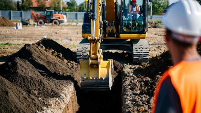 Багер извършва изкопни работи за полагане на траншеи за водоснабдителни и канализационни системи.
